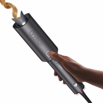 Hand using an automatic hair curler on brown hair.